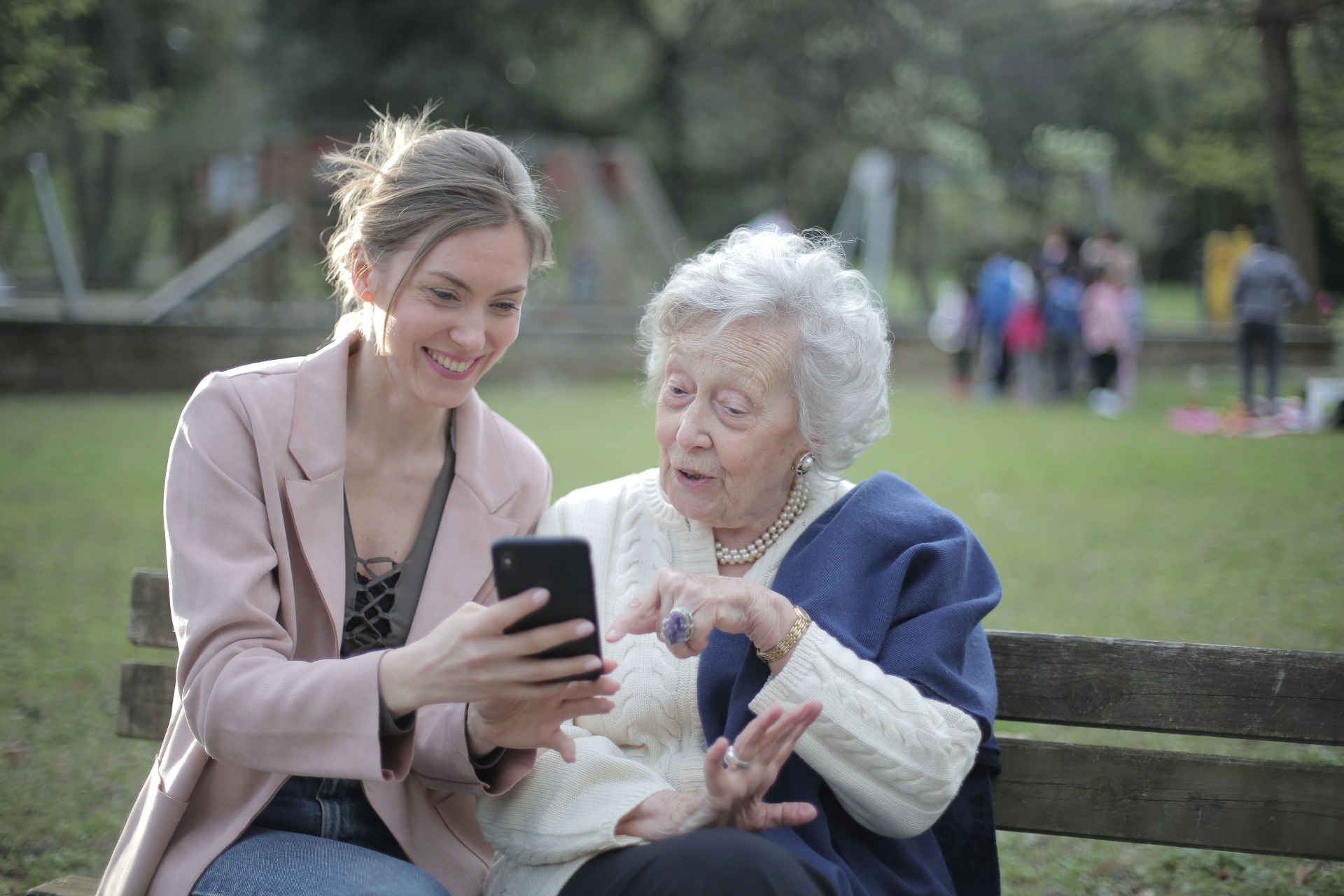 An adult daughter sharing a phone with her elderly mother on a park bench